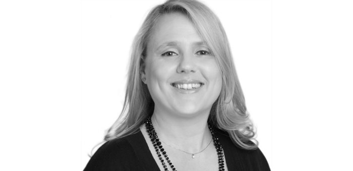 Black and white headshot of a smiling woman with shoulder-length hair, wearing a necklace, against a plain background.