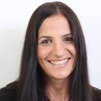 Headshot of a smiling woman with long straight brown hair and a white top, against a light background.