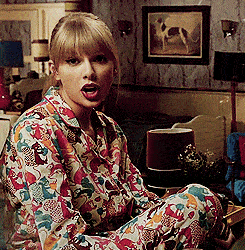 Woman in patterned pajamas working from home, sitting on the floor and playfully sticking out her tongue, with vintage decor in the background.