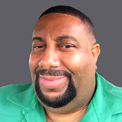 A man with a short haircut and a goatee, wearing a green shirt, smiles slightly in front of a plain grey background. - SysAid