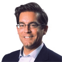 Professional headshot of a smiling man wearing glasses, a dark blazer, and a blue shirt against a light background.