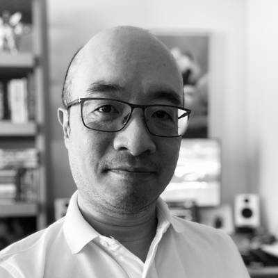 Black and white portrait of a bald man with glasses, wearing a white shirt, looking directly at the camera.