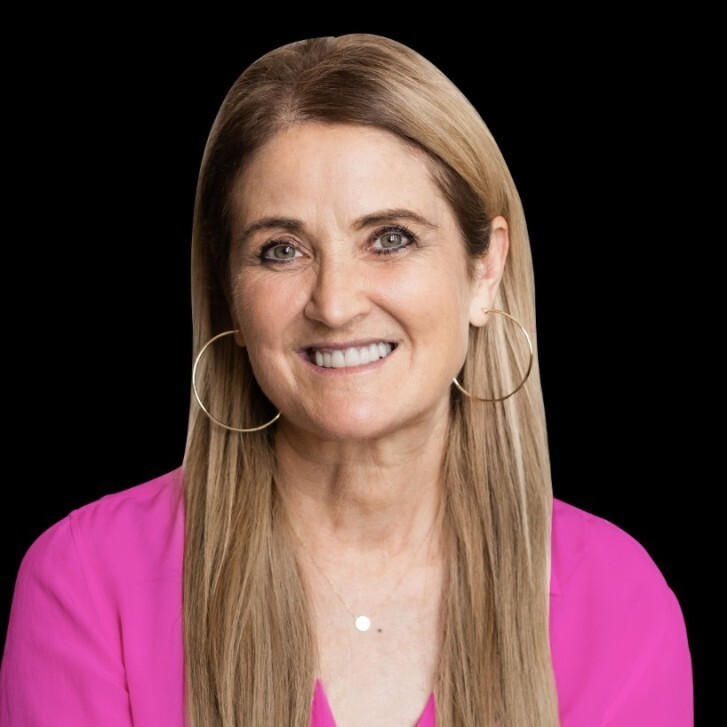 A smiling woman with long brown hair wearing a bright pink blouse and large hoop earrings against a black background.