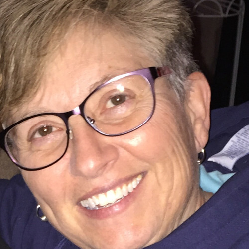 Close-up of a smiling woman with short hair, wearing glasses and a navy blue top.