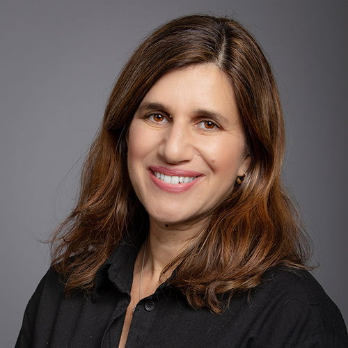 Professional headshot of a smiling woman with medium-length brown hair, wearing a black blouse, against a gray background.
