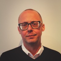 Professional man in smart attire stands against a plain background, representing SysAid’s ITSM expertise. - SysAid