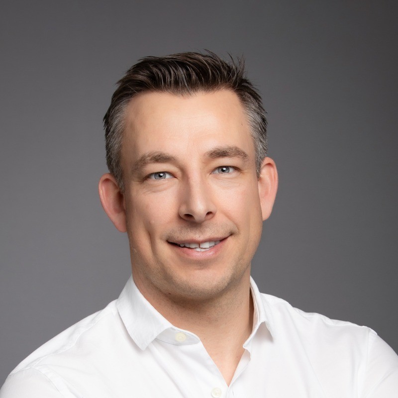 A man in a white shirt poses for a headshot against a gray background. - SysAid