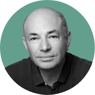 Portrait of a middle-aged bald man with a gentle smile, wearing a dark shirt against a teal background.